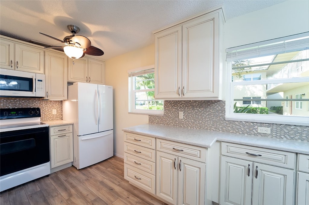 kitchen featuring a textured ceiling, ceiling fan, backsplash, light hardwood / wood-style flooring, and white appliances