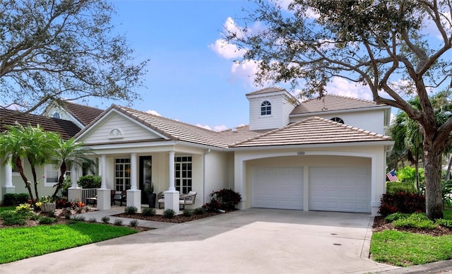 view of front of property with a garage, covered porch, driveway, a tiled roof, and stucco siding