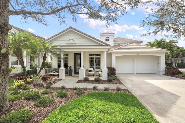 view of front of property with covered porch, a garage, a tile roof, concrete driveway, and stucco siding