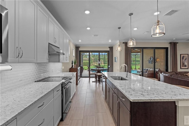 kitchen with an island with sink, decorative light fixtures, under cabinet range hood, stainless steel range with electric stovetop, and a sink