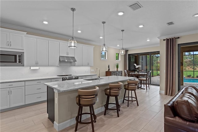 kitchen featuring a kitchen island with sink, white cabinets, open floor plan, hanging light fixtures, and appliances with stainless steel finishes