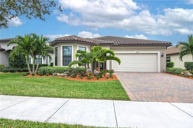 mediterranean / spanish-style home featuring a tiled roof, a front yard, stucco siding, decorative driveway, and a garage