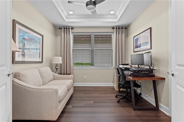 office area featuring a tray ceiling, ornamental molding, dark wood-type flooring, ceiling fan, and baseboards