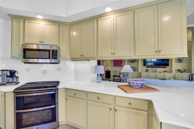 kitchen featuring stainless steel appliances, kitchen peninsula, tasteful backsplash, light stone countertops, and cream cabinetry