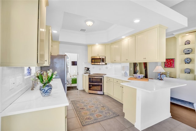 kitchen with stainless steel appliances, kitchen peninsula, light tile patterned floors, ornamental molding, and a tray ceiling