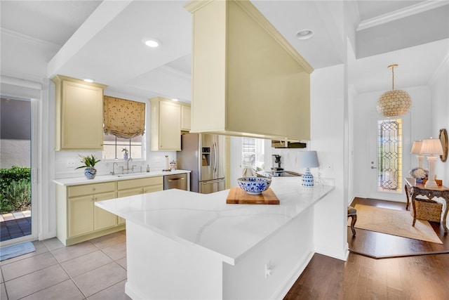 kitchen featuring stainless steel appliances, kitchen peninsula, ornamental molding, light stone countertops, and light wood-type flooring