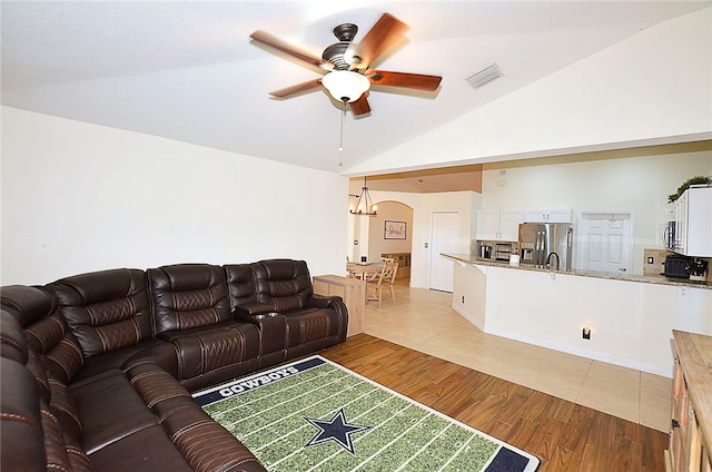 living room with high vaulted ceiling, ceiling fan with notable chandelier, and light hardwood / wood-style flooring