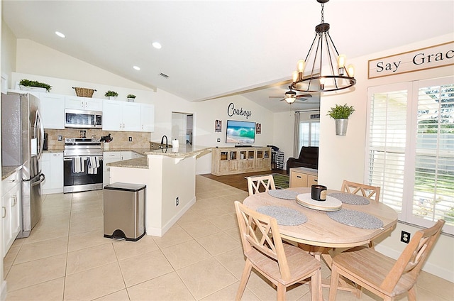 kitchen with lofted ceiling, light stone counters, hanging light fixtures, white cabinetry, and appliances with stainless steel finishes