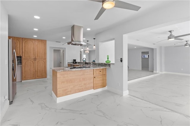 kitchen featuring light stone countertops, hanging light fixtures, island range hood, kitchen peninsula, and stainless steel fridge