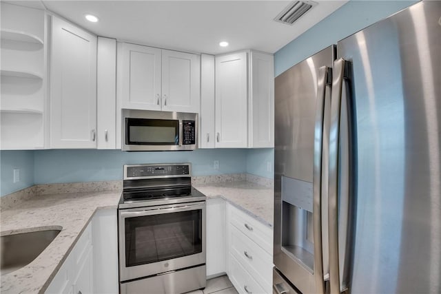 kitchen featuring light stone countertops, white cabinetry, light tile patterned flooring, and stainless steel appliances