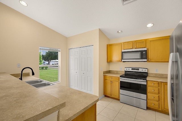 kitchen with light tile patterned flooring, sink, lofted ceiling, and stainless steel appliances