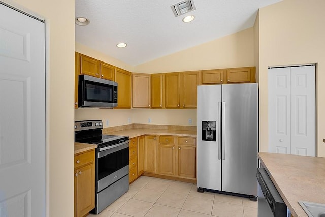 kitchen with appliances with stainless steel finishes, vaulted ceiling, and light tile patterned flooring