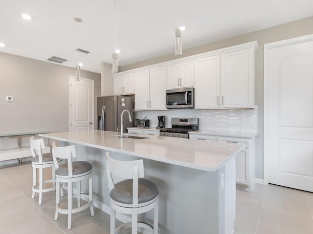 kitchen featuring decorative light fixtures, tasteful backsplash, white cabinetry, stainless steel appliances, and a center island with sink