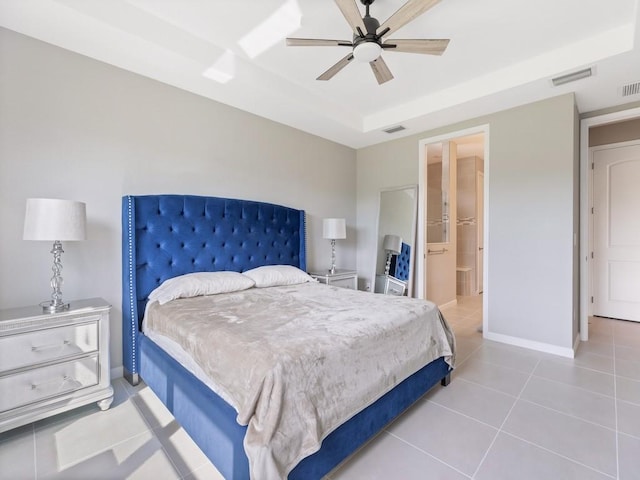 tiled bedroom featuring a tray ceiling, ensuite bath, and ceiling fan