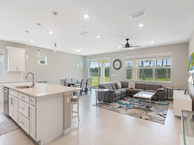 kitchen featuring an island with sink, sink, white cabinets, hanging light fixtures, and stainless steel dishwasher