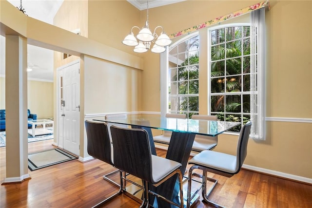 dining space with wood finished floors, baseboards, ornamental molding, and a notable chandelier