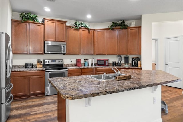 kitchen with sink, a kitchen island with sink, dark wood-type flooring, a breakfast bar area, and stainless steel appliances