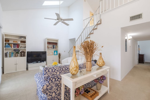 living room featuring high vaulted ceiling, a skylight, light carpet, and ceiling fan