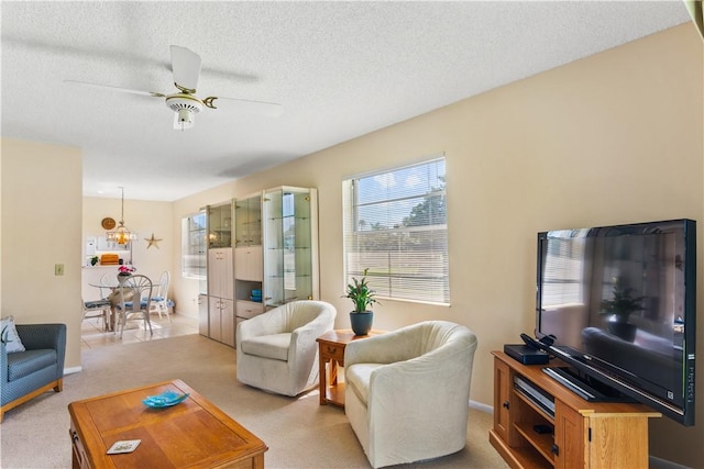 living area with light carpet, a textured ceiling, baseboards, and ceiling fan with notable chandelier