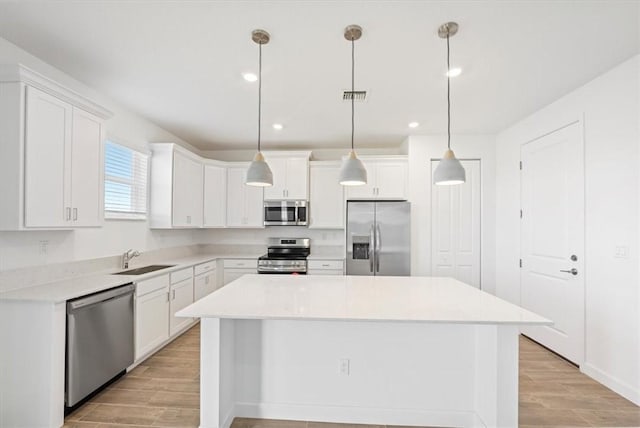 kitchen with appliances with stainless steel finishes, a sink, a center island, light wood-type flooring, and white cabinetry