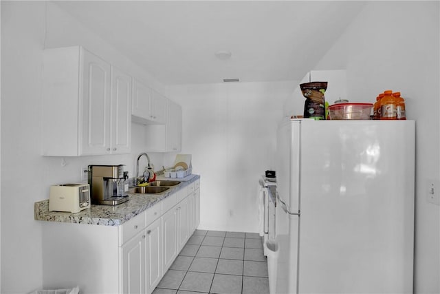 kitchen featuring light tile patterned floors, visible vents, freestanding refrigerator, a sink, and white cabinets