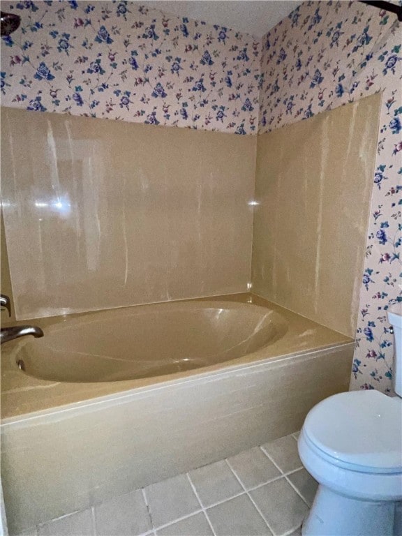 bathroom featuring a relaxing tiled tub, tile patterned flooring, and toilet