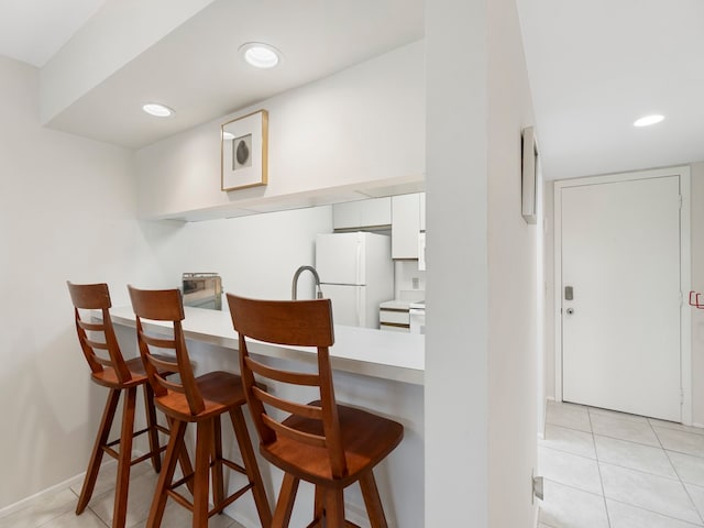 kitchen with white cabinets, light tile patterned floors, white fridge, and a breakfast bar area