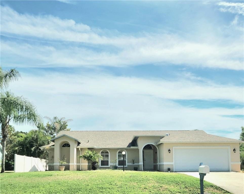 ranch-style house with a garage, fence, driveway, stucco siding, and a front lawn