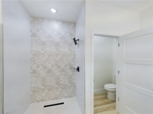 bathroom featuring a tile shower, wood-type flooring, and toilet