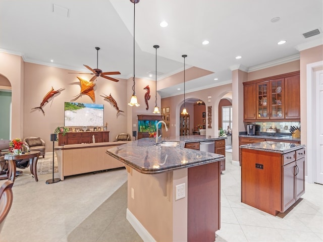 kitchen with tasteful backsplash, dark stone counters, sink, decorative light fixtures, and an island with sink