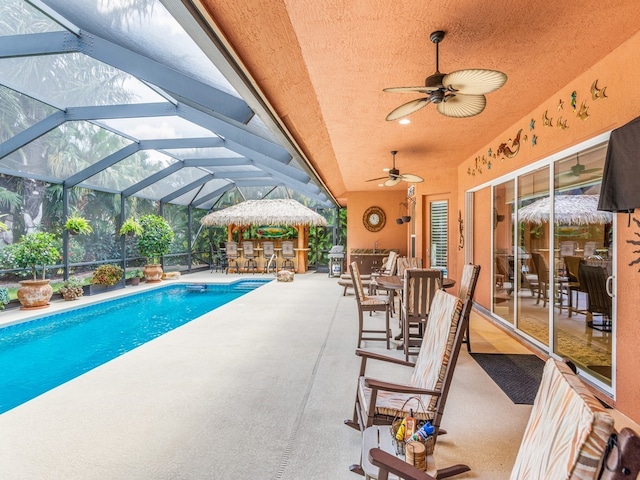 view of swimming pool with glass enclosure, an outdoor bar, ceiling fan, and a patio area