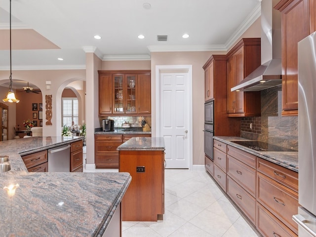 kitchen featuring a center island, wall chimney range hood, dark stone countertops, decorative light fixtures, and appliances with stainless steel finishes