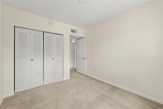 unfurnished bedroom featuring baseboards, a closet, visible vents, and light colored carpet