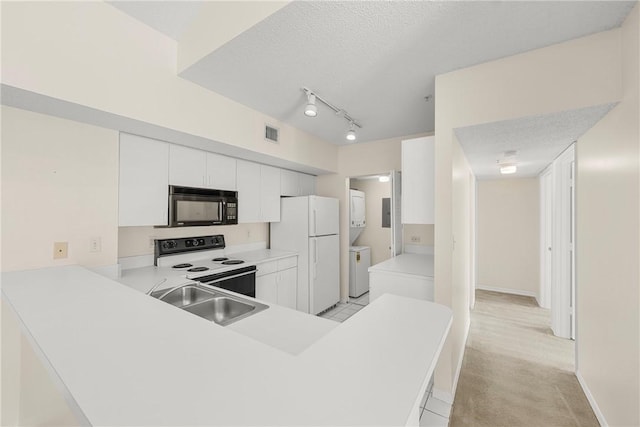 kitchen with black microwave, electric range, a sink, freestanding refrigerator, and stacked washer and clothes dryer