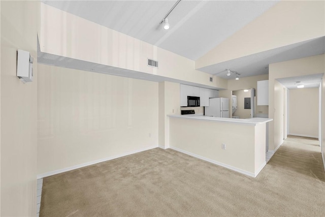 kitchen featuring black microwave, vaulted ceiling, light carpet, and freestanding refrigerator