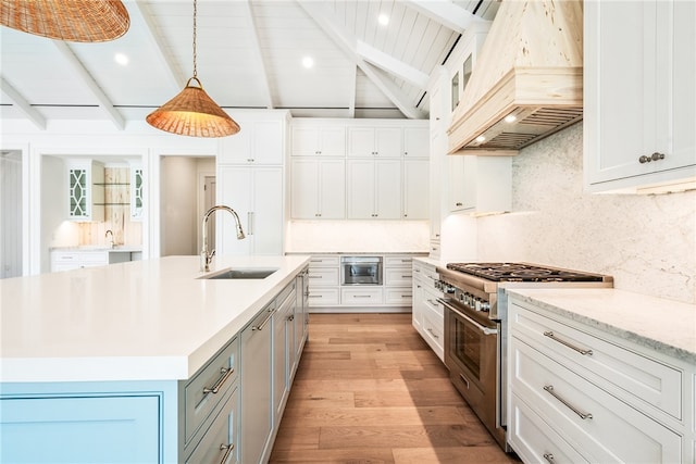 kitchen featuring high end stainless steel range, white cabinets, premium range hood, and a center island with sink