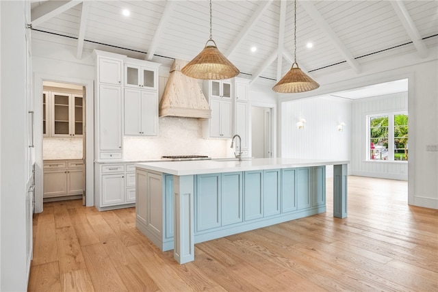 kitchen with pendant lighting, light hardwood / wood-style flooring, white cabinets, and a kitchen island with sink