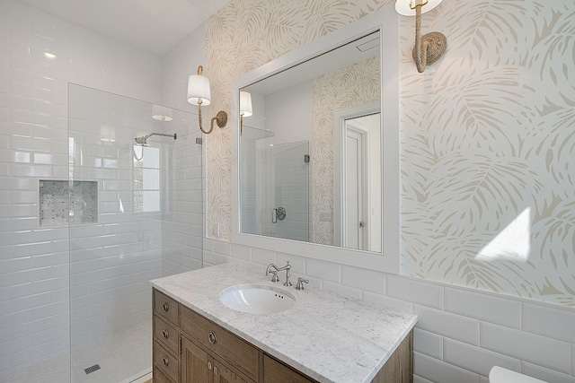 bathroom with a tile shower, vanity, and tile walls