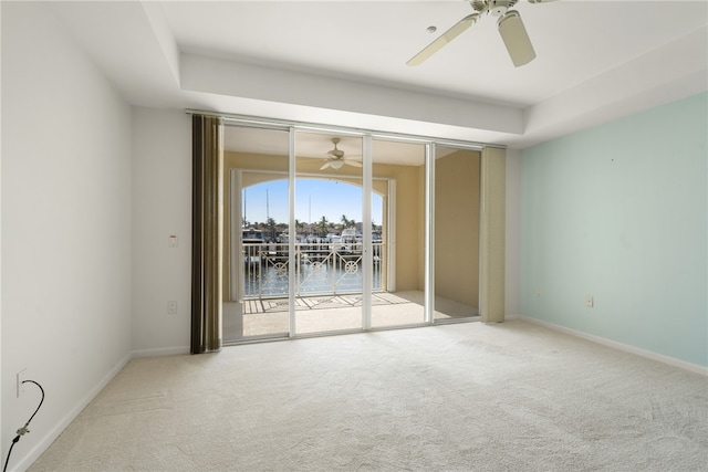 spare room with ceiling fan, carpet flooring, a water view, and a tray ceiling