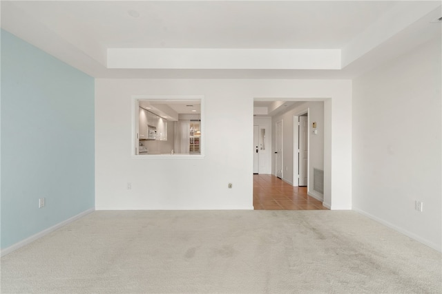 empty room with light colored carpet and a raised ceiling