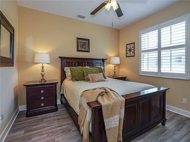 bedroom with a ceiling fan, visible vents, baseboards, and wood finished floors