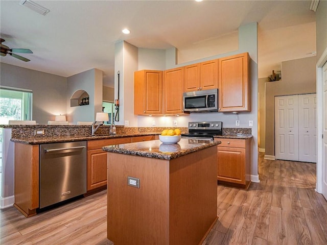 kitchen with light wood-style floors, a kitchen island, dark stone counters, and stainless steel appliances