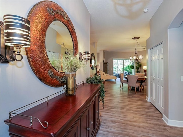 corridor with baseboards, an inviting chandelier, and wood finished floors