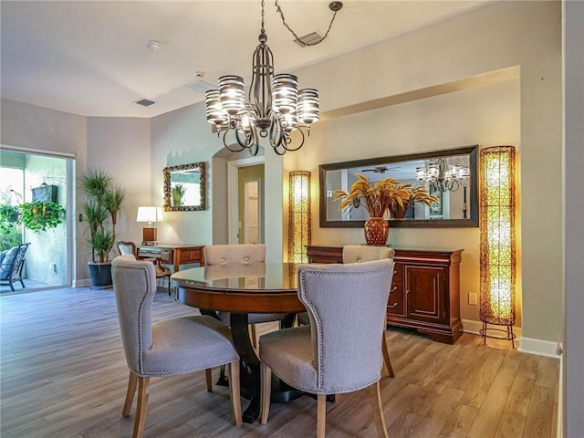 dining area with baseboards, light wood finished floors, visible vents, and an inviting chandelier