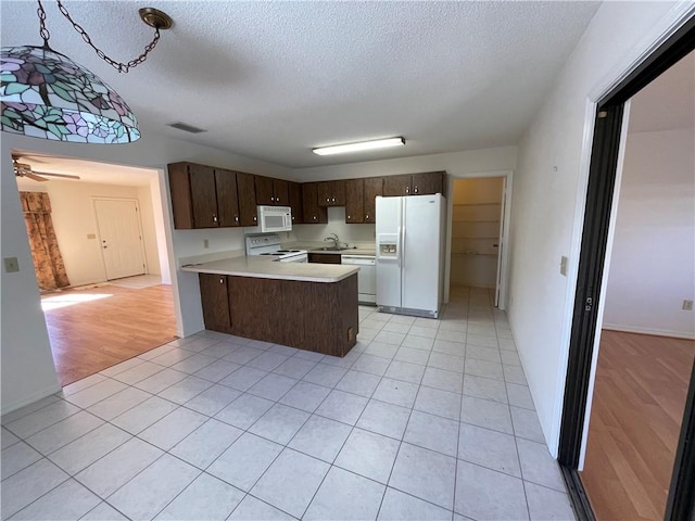 kitchen with sink, decorative light fixtures, dark brown cabinets, kitchen peninsula, and white appliances