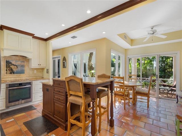 kitchen with stainless steel oven, crown molding, ceiling fan, light stone countertops, and tasteful backsplash