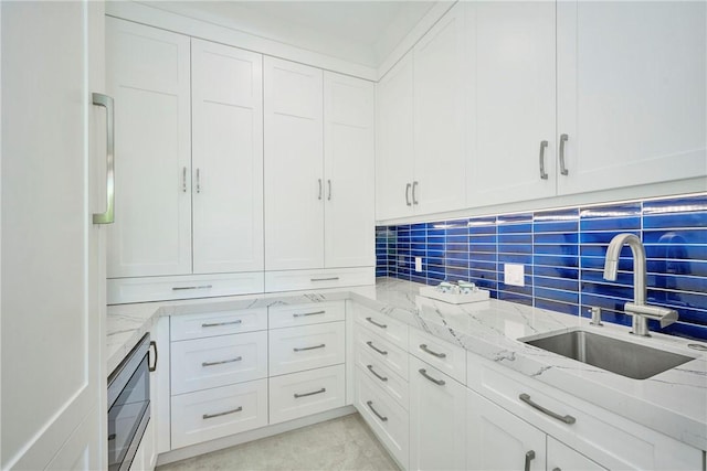 kitchen with decorative backsplash, light stone counters, white cabinetry, and a sink