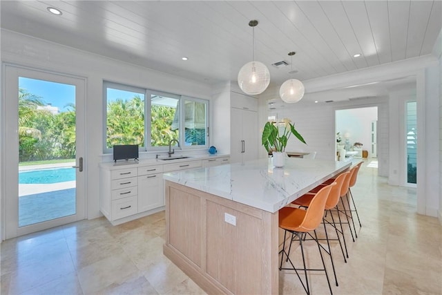 kitchen featuring a sink, wooden ceiling, a kitchen breakfast bar, and light stone countertops