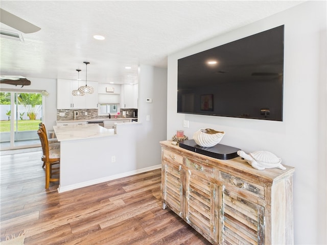 249 Columbus St, Sebastian, FL 32958 - kitchen featuring white cabinets, light wood finished floors, light countertops, backsplash, and a peninsula