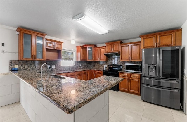 6057 Ridge Lake Cir, Vero Beach, FL 32967 - kitchen featuring stainless steel appliances, a peninsula, brown cabinetry, dark stone counters, and under cabinet range hood